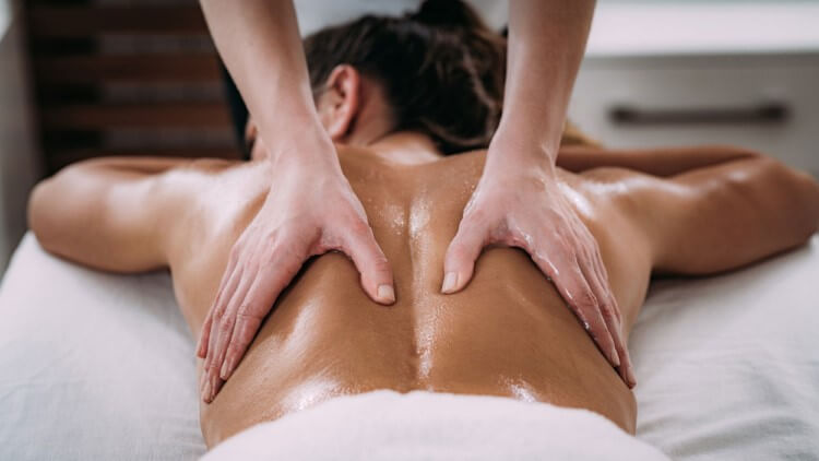 A man with his eyes closed lying on his stomach resting his head on his hands while someone‘s hands massage his back.